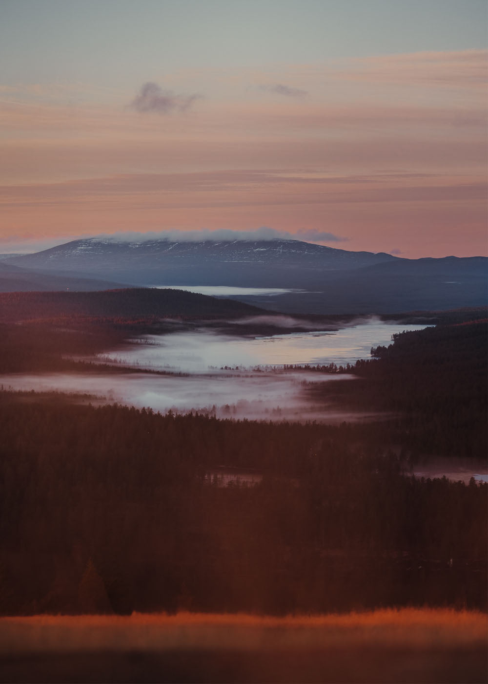 Höstlandskap med sjöar och skogar i varma färgtoner, med snötäckta berg i bakgrunden under en rosa-orange himmel.Poster i olika storlekar: 30x40 cm, 40x50 cm, 50x70-cm, 70x100 cm.