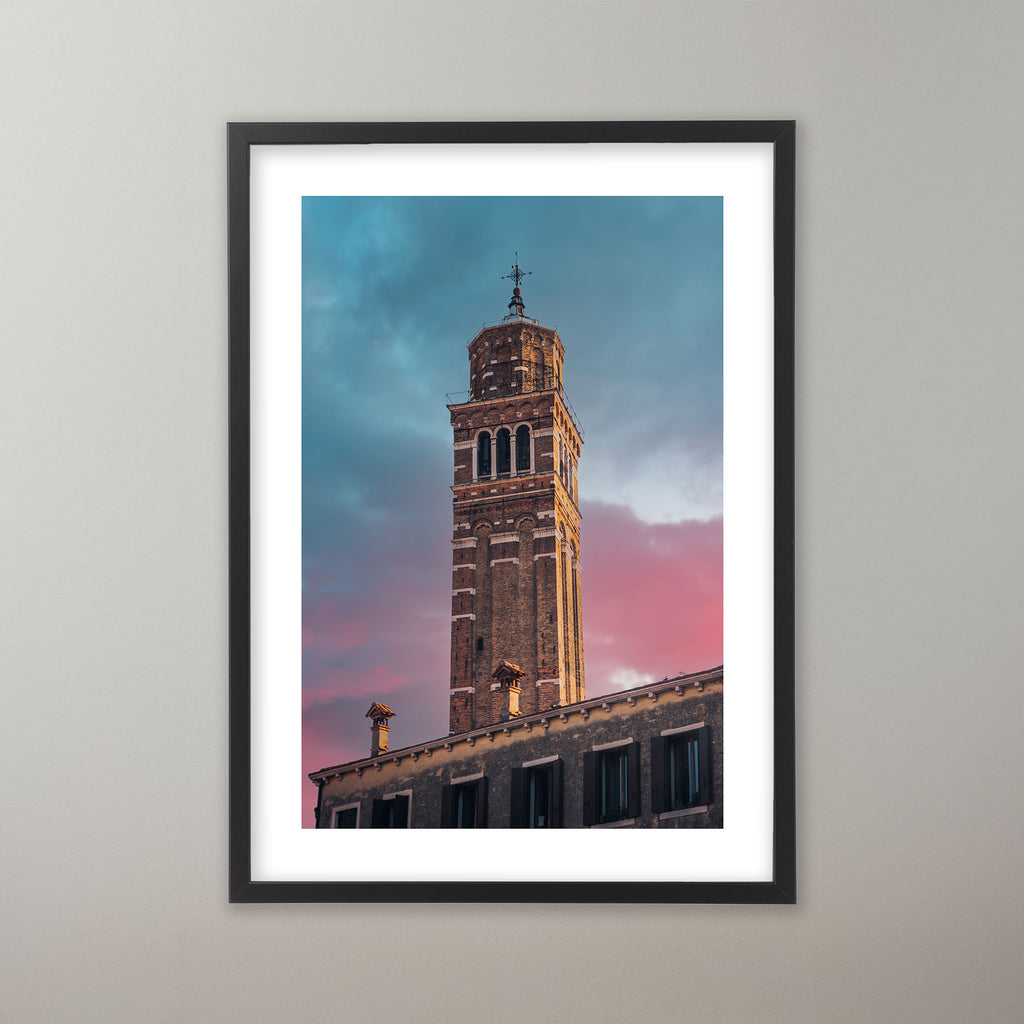Venetianskt klocktorn i rödbrunt tegel mot en dramatisk himmel i skymningen med färgskiftningar från blått till rosa. Poster i olika storlekar: 30x40 cm, 40x50 cm, 50x70-cm, 70x100 cm.